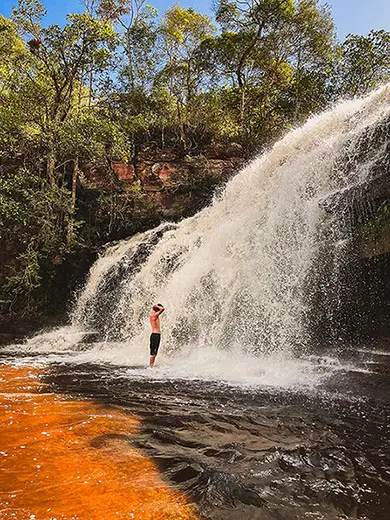 Visitante toma banho na Cachoeira da Altina, parte do rio Funis, no Vale do Pati, vegetação e montanhas ao fundo.