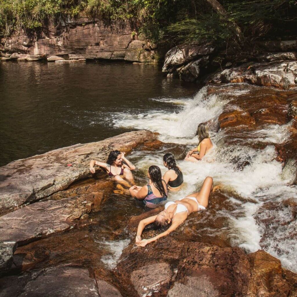 Mulheres tomam banho de Cachoeira nas quedas do rio Funis, no Vale do Pati. Poço para banho ao fundo com vegetação ao redor.